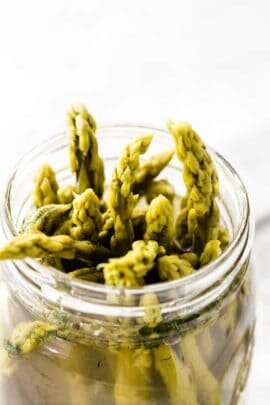 The tops of pickled asparagus peeking out of a canning jar