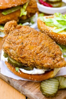 Crispy chicken sandwich on a wooden board with pickles on the side