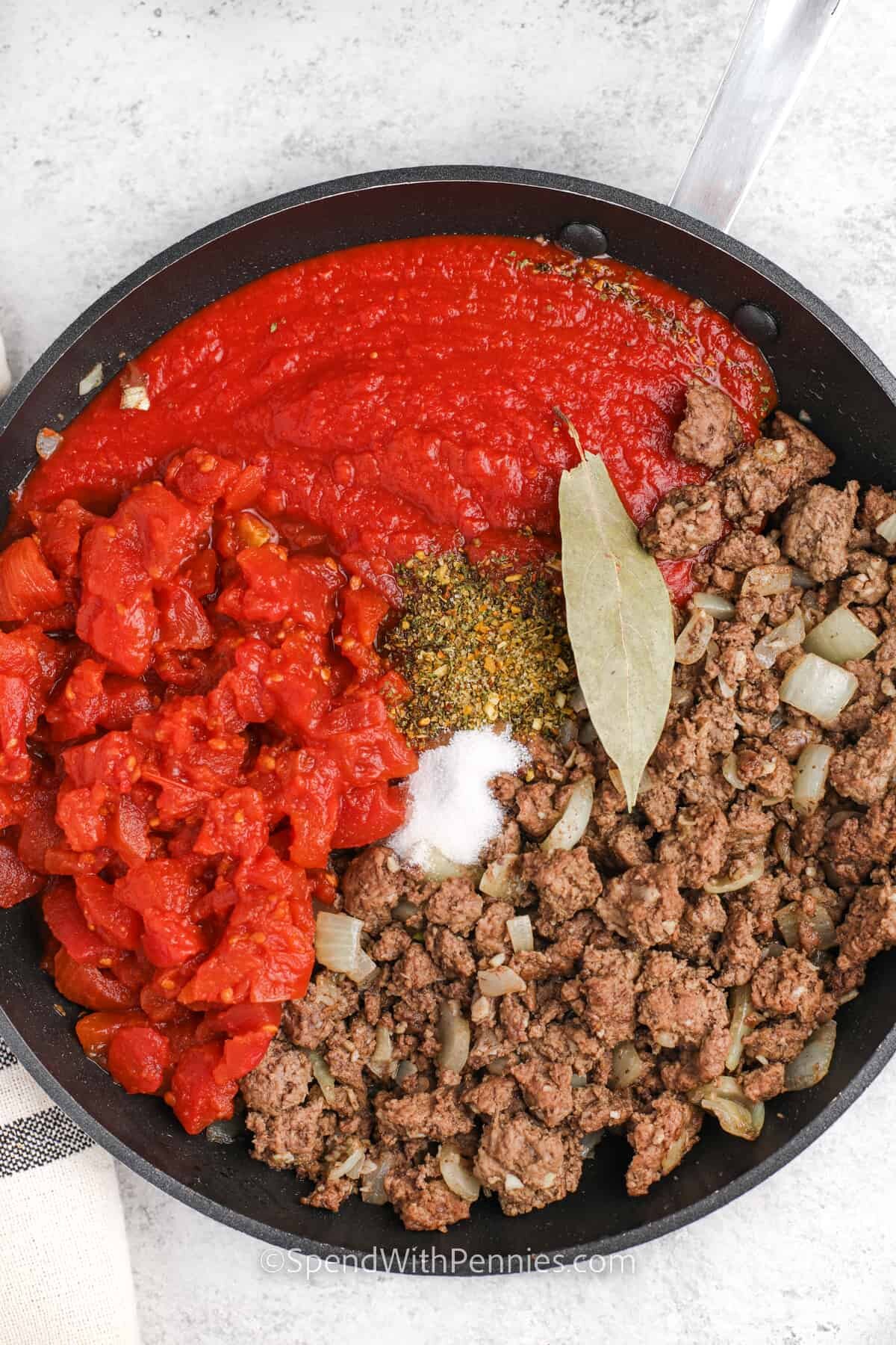 adding tomatoes and seasoning to beef mixture to make Zucchini Lasagna