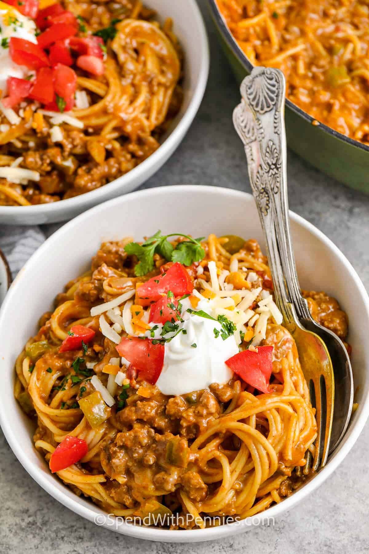 a bowl of taco spaghetti topped with sour cream and tomatoes.